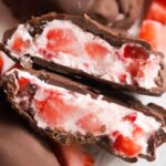 Close-up of a chocolate-covered strawberry dessert cut in half, showing fresh strawberry pieces mixed with a creamy white filling inside a rich chocolate coating.