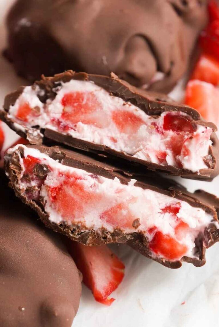 Close-up of a chocolate-covered strawberry dessert cut in half, showing fresh strawberry pieces mixed with a creamy white filling inside a rich chocolate coating.