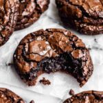 A close-up of a fudgy chocolate cookie with a cracked top, sprinkled with sea salt, and a bite taken out of it.