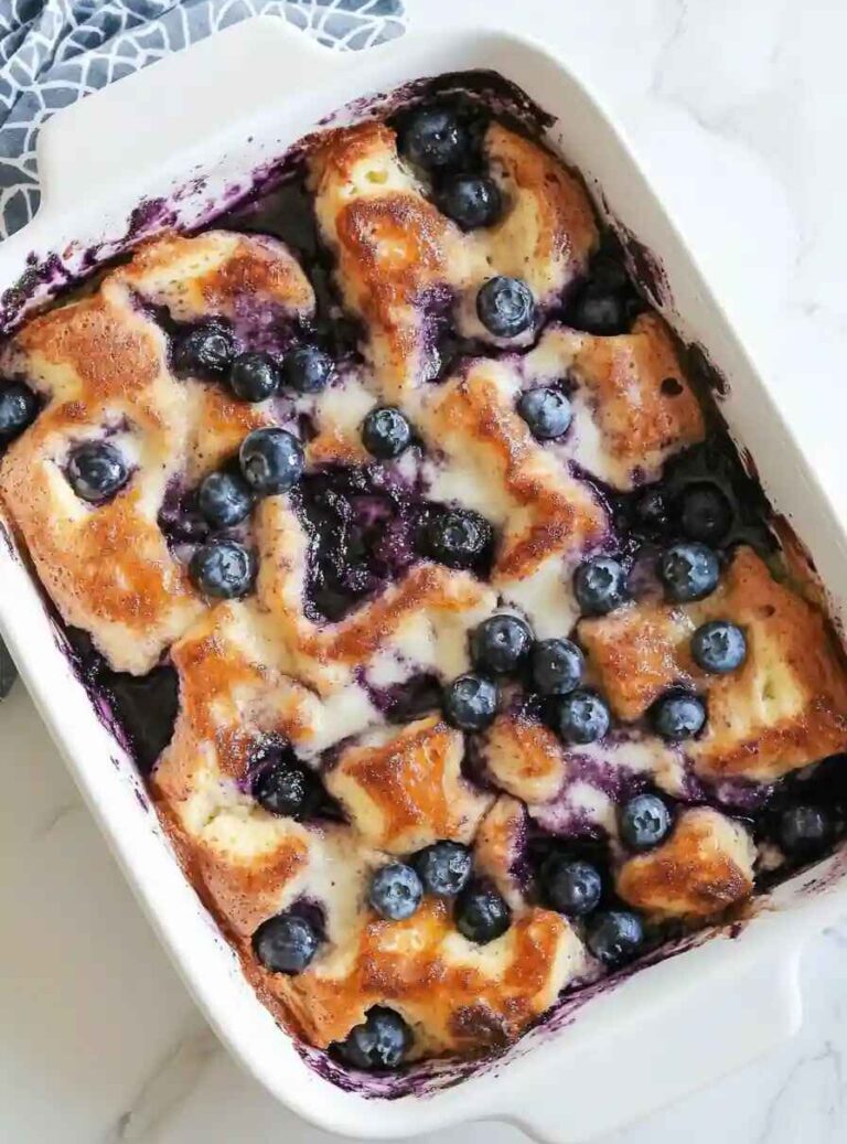 Freshly baked blueberry bread pudding topped with golden brown crust, melted cream, and juicy blueberries in a white baking dish