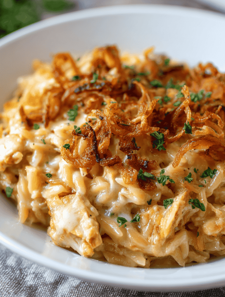 Creamy French Onion Chicken Orzo Casserole baked with cheese and crispy fried onions in a white casserole dish.