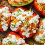 Dairy-free buffalo chicken stuffed bell peppers garnished with fresh herbs on a white plate