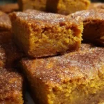 A stack of soft pumpkin snickerdoodle blondies dusted with cinnamon sugar, showing their moist, golden-orange texture and chewy edges.