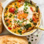 Creamy baked feta eggs in a white dish topped with olive oil and fresh herbs