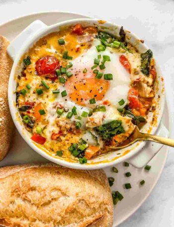 Creamy baked feta eggs in a white dish topped with olive oil and fresh herbs