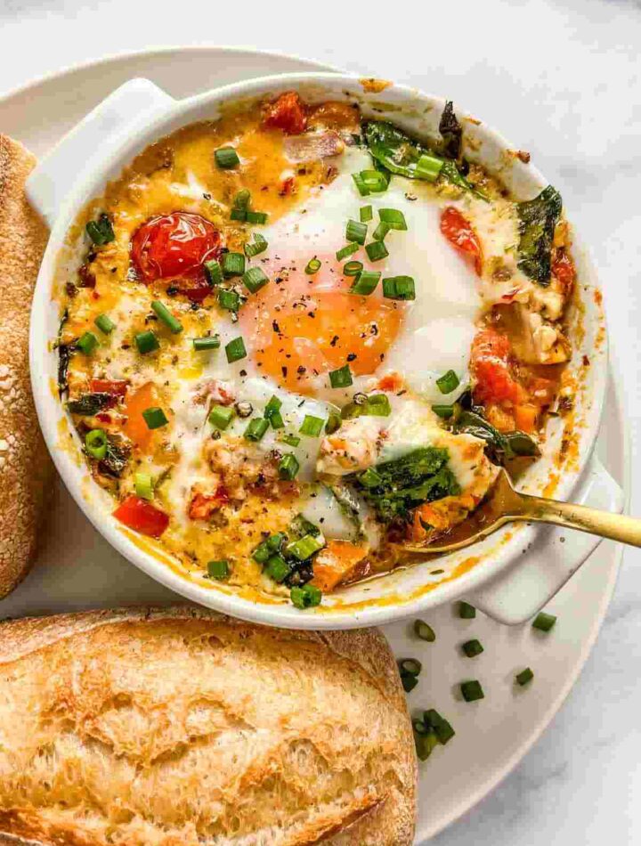 Creamy baked feta eggs in a white dish topped with olive oil and fresh herbs