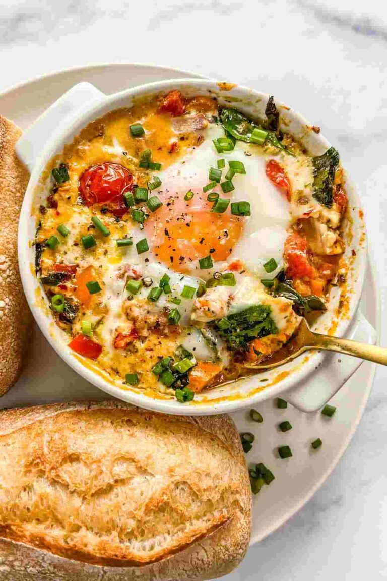 Creamy baked feta eggs in a white dish topped with olive oil and fresh herbs